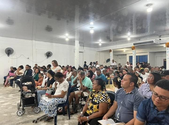 Imagen fotorrealista de un grupo diverso de personas de todas las edades y orígenes sonriendo e interactuando, con una cálida iluminación en un entorno de iglesia moderno. Concéntrese en sus expresiones alegres e interacciones genuinas. Use una profundidad de campo reducida para resaltar a las personas, con un fondo de iglesia ligeramente borroso. Capture una sensación de bienvenida, inclusión y experiencia compartida. Utilice una paleta de colores cálida y acogedora con iluminación natural.